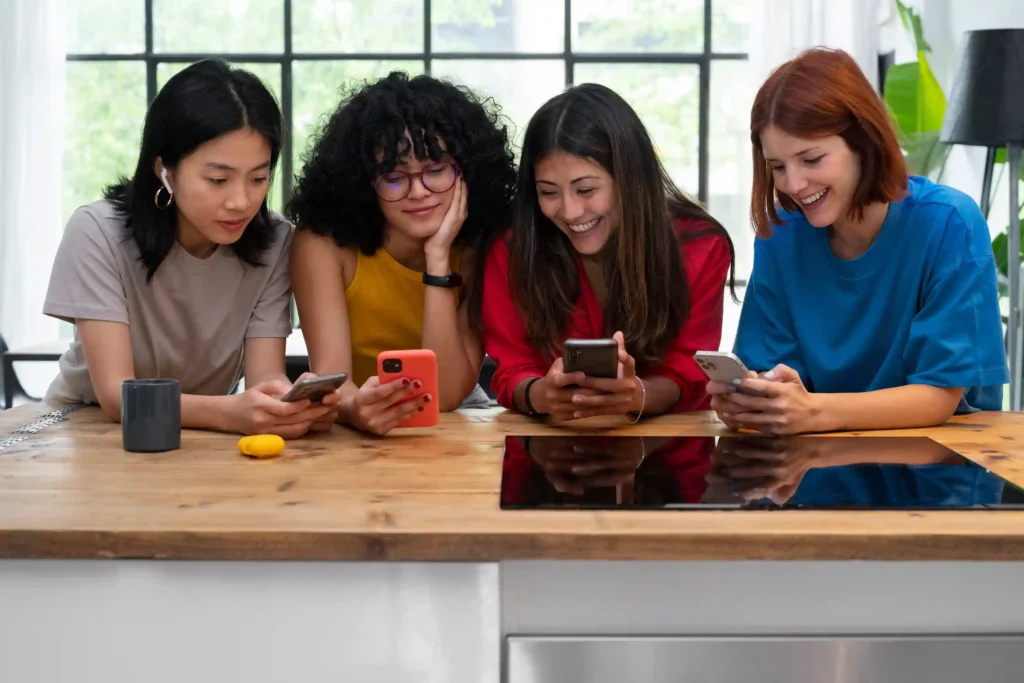 Four women sitting at a table and focused on their smartphones, representing the rise of skilled female technicians and diversity in the mobile phone repair field