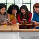 Four women sitting at a table and focused on their smartphones, representing the rise of skilled female technicians and diversity in the mobile phone repair field