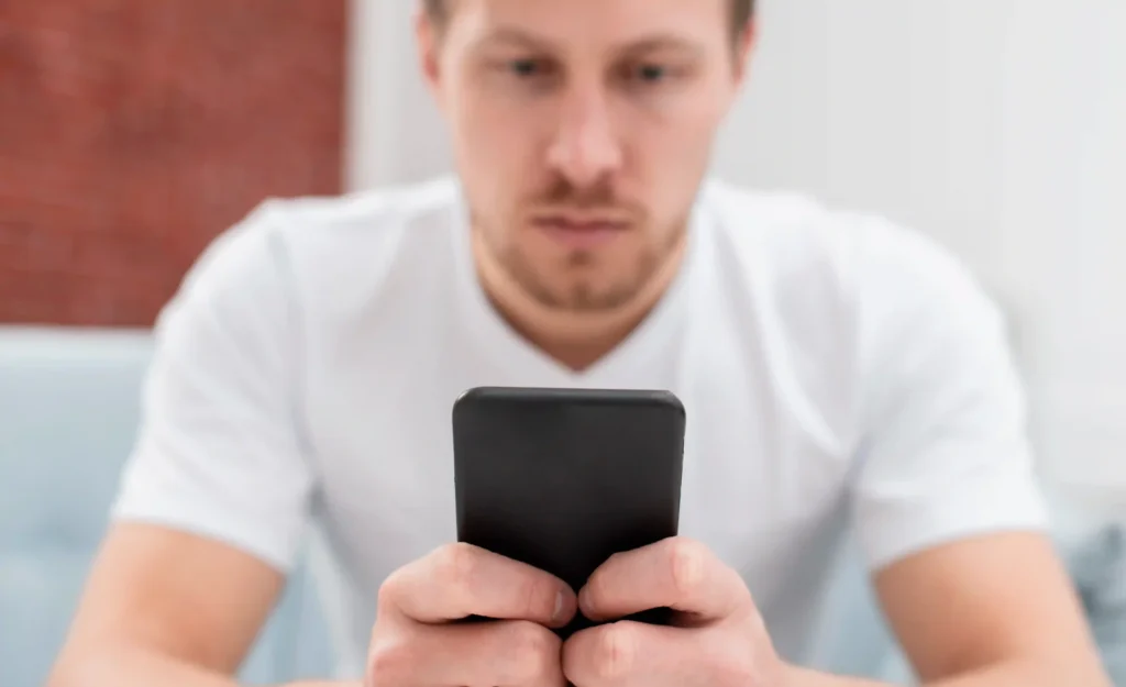 Man in a white shirt intently holding and scrolling on a smartphone, representing uncertainty about updating Android on his device